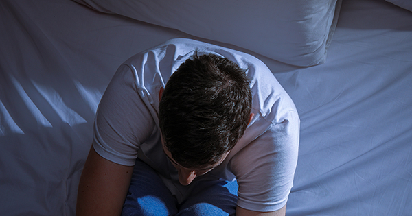 Man sat on a bed with his head in his hands